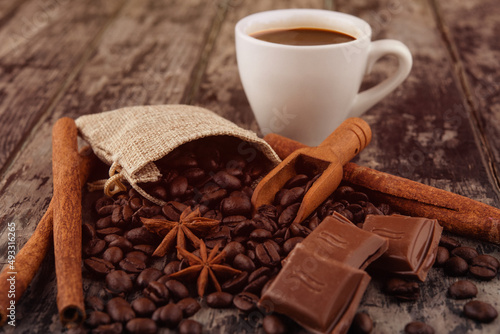 cup of coffee with chocolate, cinnamon sticks, and coffee beans on wooden background