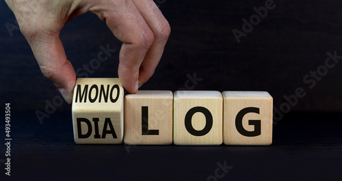 Businessman turns wooden cubes and changes the German word monolog - monologue in English to dialog - dialogue in English. Beautiful grey background. Business monolog or dialog concept. Copy space.