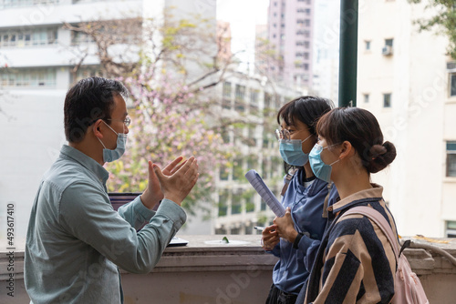 university or college male teacher with face mask explains to asian female students during field test beyond classroom in university in Hong Kong during covid-19