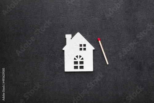 White house shape and matchstick on dark black background. Closeup. Concept of home protection or loss from fire. Top down view.