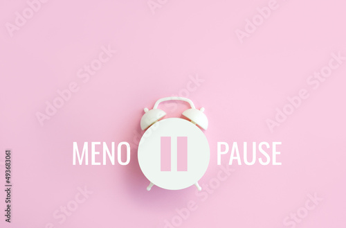 Word Menopause, pause sign on a white alarm clock on pink background. Minimal concept hormone replacement therapy. Сopy space