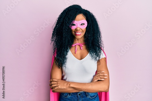 Middle age african american woman wearing super hero costume happy face smiling with crossed arms looking at the camera. positive person.