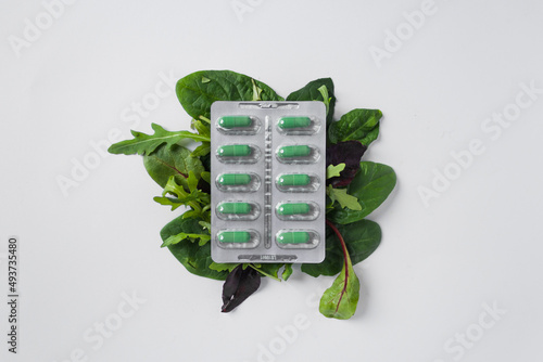 Silver blister with diet supplements in green capsules on the green leaves of arugula and lettuce. Health care concept.