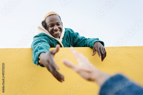 Black African Man helping caucasian friend offering hand to climb wall. Concept of, friendship, solidarity and support