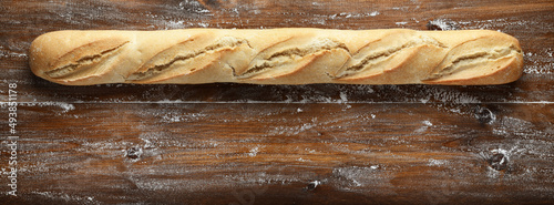 Whole baguette on wooden background, top view, space for text.