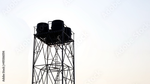 Silhouette of a water tank on a tower. Spare water tank on metal structure on white-blue sky background with copy space. Selective focus