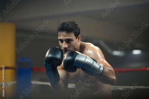 Young boxer attacking competitio in ring during competition. Focused shirtless man in boxing gloves preparing for hitting. Fighter concept