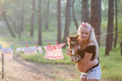 Smiling Latvian pregnant woman carrying her dog with baby laundries background