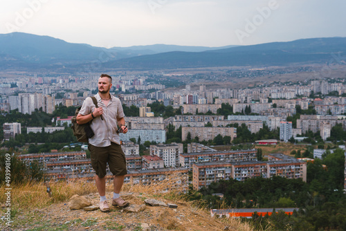 A tourist with backpack poses against the backdrop of a densely populated area. Wretched high-rise buildings, dark gloomy tones. Copy space. Tbilisi Georgia. Zghvisubani III Micro-District