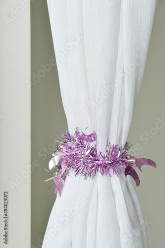 White voile curtain wrap around by a purple party tinsel