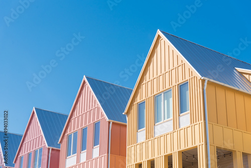 Lookup view of metal roof and gutter on row of new development colorful house with clear blue sky background