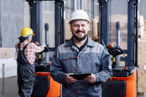 Successful mature male picker or quality control manager with tablet standing in front of camera against his female coworker