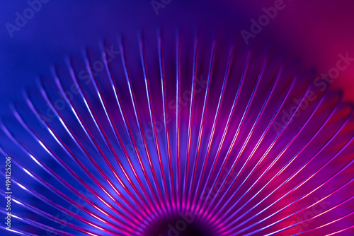 Closeup of coiled metal spring with sufficiently high strength and elastic properties in neon blue and red light. Macro photo, selective focus.
