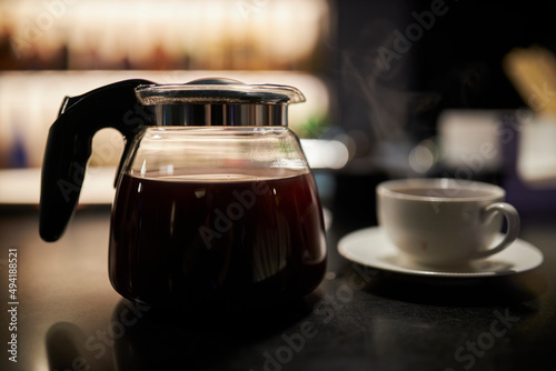 a glass teapot with filter coffee and a cup stand on the bar. Close-up of a teapot with a black coffee filter and a transparent empty glass standing on a bar counter in a cafe.