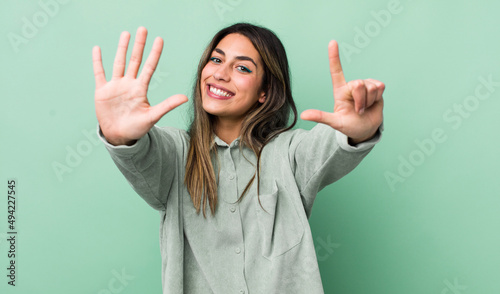 pretty hispanic woman smiling and looking friendly, showing number seven or seventh with hand forward, counting down