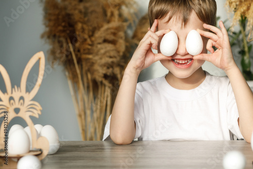 A cheerful child closes his eyes with eggs that he has prepared for the Easter holiday, symbols of the holiday for creativity