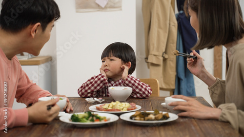 picky Asian boy shaking head while refusing food his father and mother put in his bowl during lunch time in dining room at home