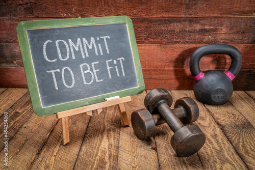 commit to be fit - inspirational concept, white chalk text on a slate blackboard sign against weathered rustic wood with a dumbbells and kettlebell