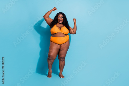 Full length portrait of curvy figure obesity lady raise fists achieve luck enjoy herself no filters isolated on blue color background