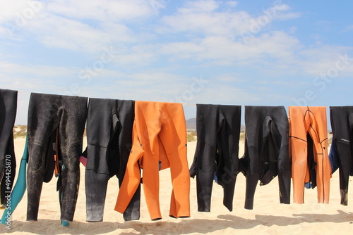 Colorful wetsuits hanging on a rope to dry in the sun at the beach 