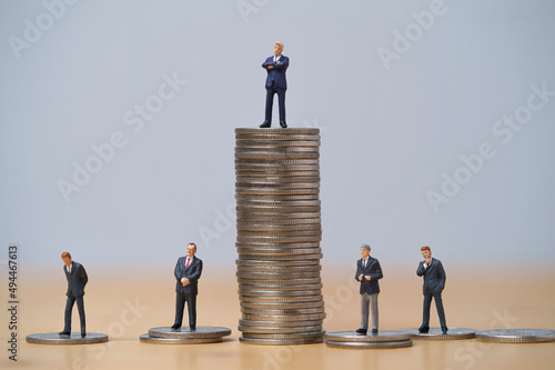 Miniature figure of five businessmen standing to different high and low coins stacking for position and successful business investment income concept.