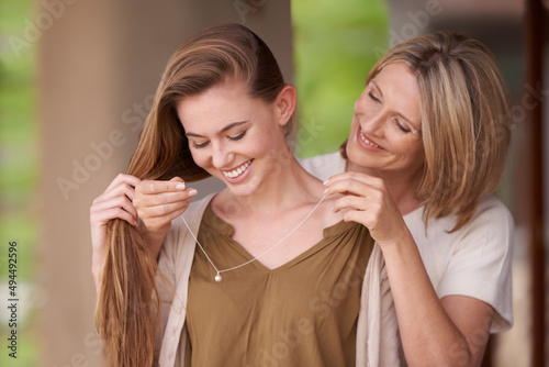 I want you to have this.... A mother lovingly putting a necklace around her daughters neck.