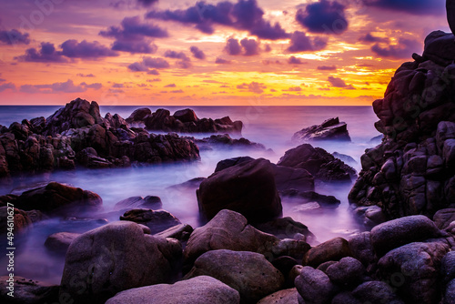 fotografía de larga exposición en atardecer en el mar con un cielo rojo con nubes purpuras y efecto del movimiento de las olas entre las rocas de la playa coral de puerto escondido Oaxaca México