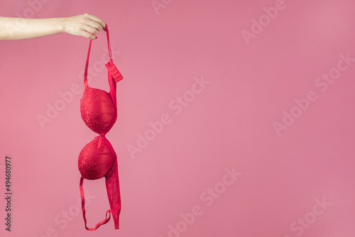 A woman's hand holding a red bra on a pink background. The concept of women's breasts, underwear. Copy space