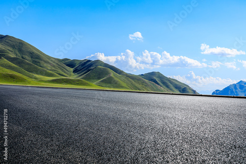 Empty asphalt road and green mountain under blue sky
