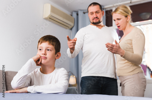 Frustrated boy sitting at home while parents berating him