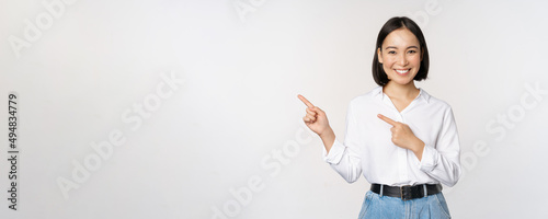 Image of smiling young office lady, asian business entrepreneur pointing fingers left, showing client info, chart of banner aside on copy space, white background