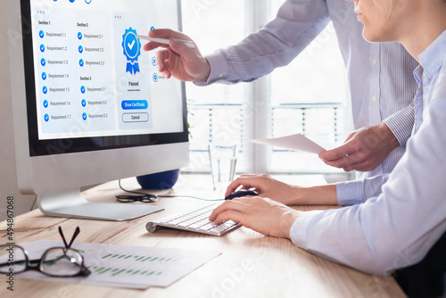 Quality Assurance (QA) and Control (QC) management. Standardization and certification concept. Compliance to international ISO standards. Manager and auditor looking at certificate on computer screen.