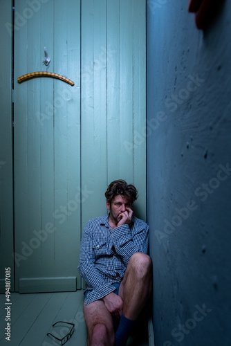 Verwirrter ungepflegter Mann mit Depressionen und Dreitagebart sitzt hilflos und einsam in der Ecke eines Zimmer. 