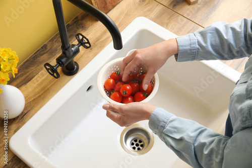 Woman washing cherry tomatoes in colander over sink, closeup