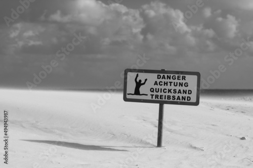 Grayscale shot of the warning sign about quicksand on the beach on a sunny day