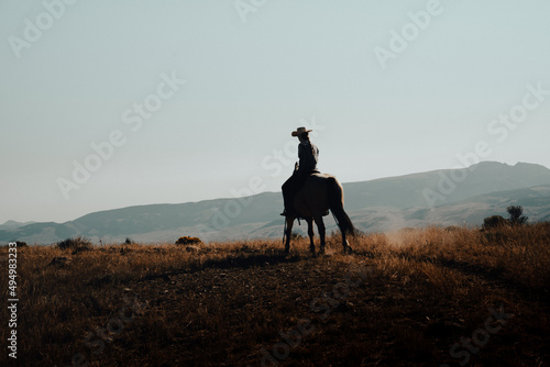 Silhouette of a cowgirl on a rural hill at sunset in Wyoming