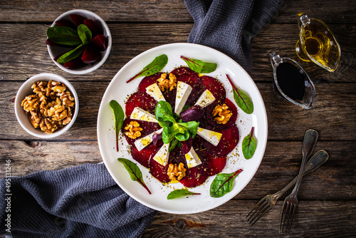 Beetroot carpaccio with goat cheese, greens and walnuts on wooden background 
