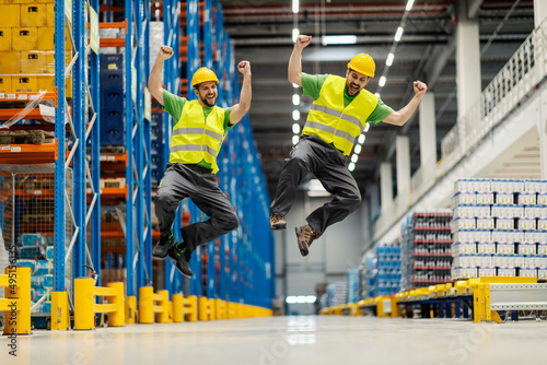 Two warehouse workers jumping and celebrating success.