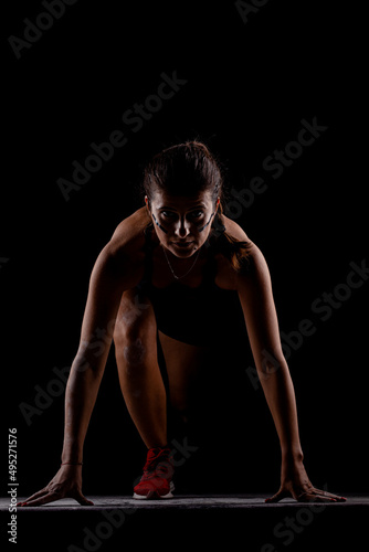 Side lit silhouette fit girl in race start position against dark background..
