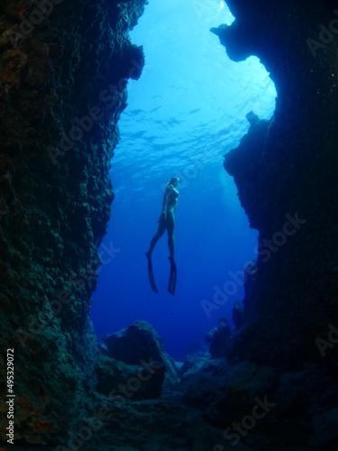 woman lady free diving apnea underwater in a cave cave with nice blue ocean scenery