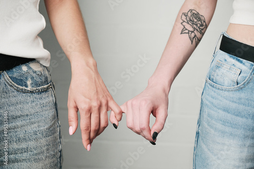 Close-up of unrecognizable lesbians holding pinkie fingers together as symbol of love