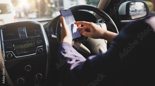 Businessman in car typing text on mobile phone to send text message while driving. Man using mobile phone looking at map while driving. Road safety and carelessness concepts.