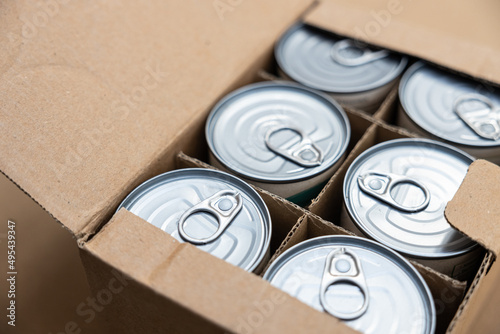 Food cans in an open cardboard box. Concept image for supply chain disruption, food shortage, stockpiling in times of war. Selective focus.