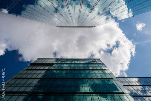 Widok na biznesowe drapacze chmur z dolnej perspektywie patrzac w niebo. Widoczne odbicia szkla w barwach niebieskich oraz zielonych