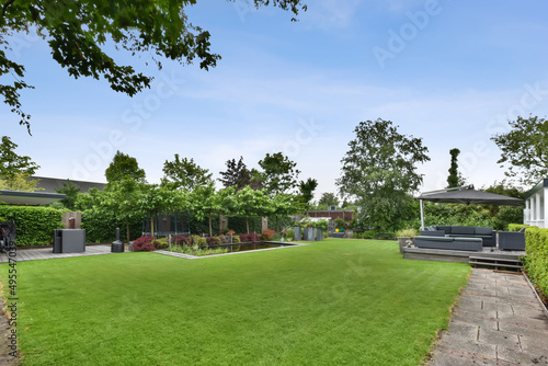 The backyard of the house with a large green lawn, a small swimming pool and a sitting area on a wooden floor