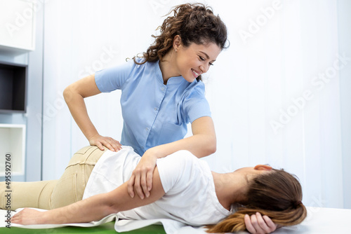 Young doctor chiropractor or osteopath fixing lying womans back with hands movements during visit in manual therapy clinic. Professional chiropractor during work