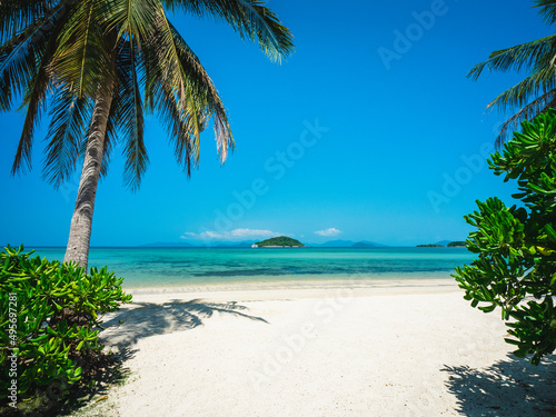 Scenic view of Koh Mak Island's peaceful crystal clear turquoise water bay with coconut palm tree foreground and Koh Kham Island at horizon. Koh Mak Island, Trat, Thailand.