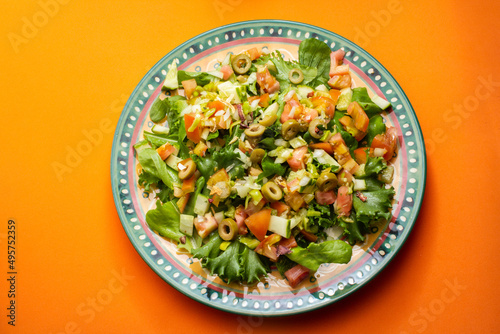 Um prato com salada de vegetais frescos sobre superfície de cor alaranjada.