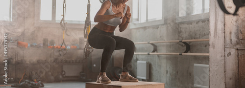 Shot of female athlete jumping on wood box during sport training in fitness center