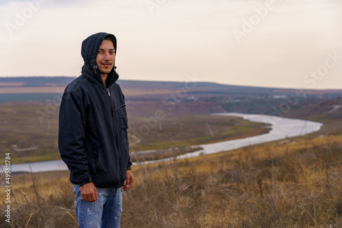 smiling man hiker in a windbreaker at dawn in a good mood. Portrait on a blurred background of nature and water